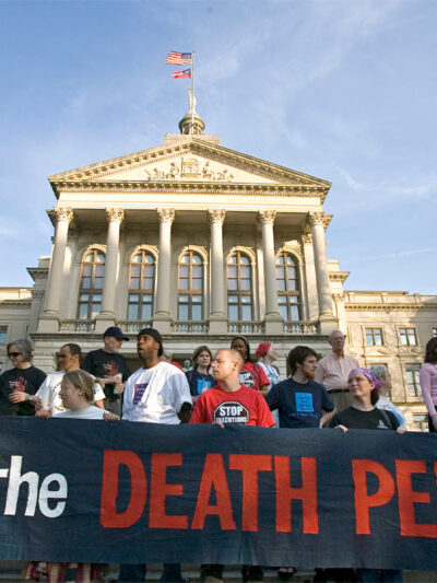 Demonstrators, holding a sign reading "STOP THE DEATH PENALTY", stand on the steps of the State Capitol in Atlanta.