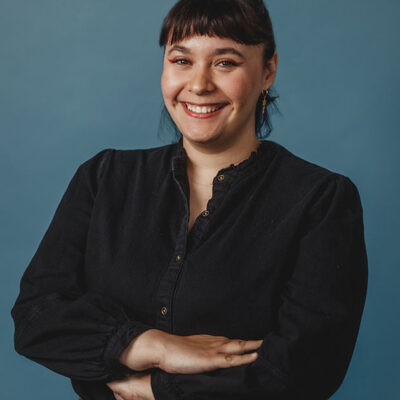 a woman with dark hair wearing a dark shirt with a blue background