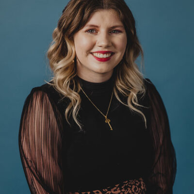 A woman with blonde hair wearing a black dress with a blue background.