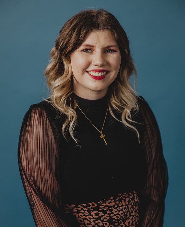 A woman with blonde hair wearing a black dress with a blue background.