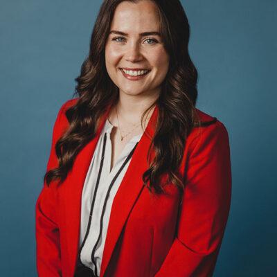 A woman with dark hair wearing a white and black striped shirt under a red jacket.