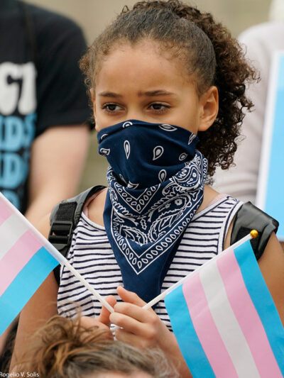 A black child holding two transgender flags
