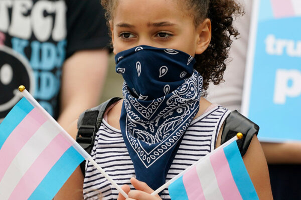 A black child holding two transgender flags
