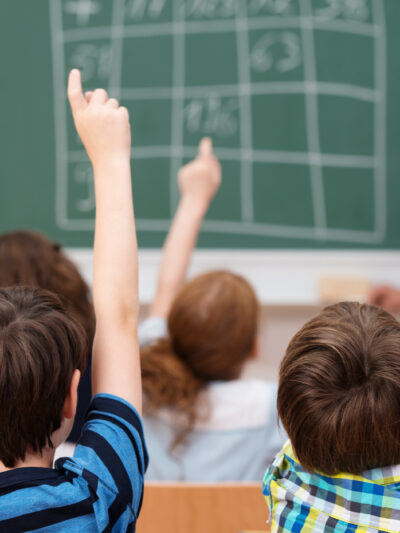 Middle school students raising hands to answer teacher.