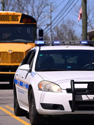A police car driving on a road in front of a school bus.