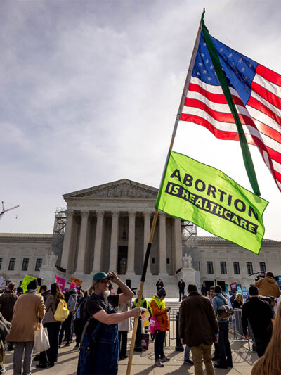 A demonstrator holds up a pole with an American flag on top and another flag reading "ABORTION IS HEALTHCARE" below it as others protest the proposed limited use of mifepristone outside the U.S. Supreme Court on the 26th of March 2024.