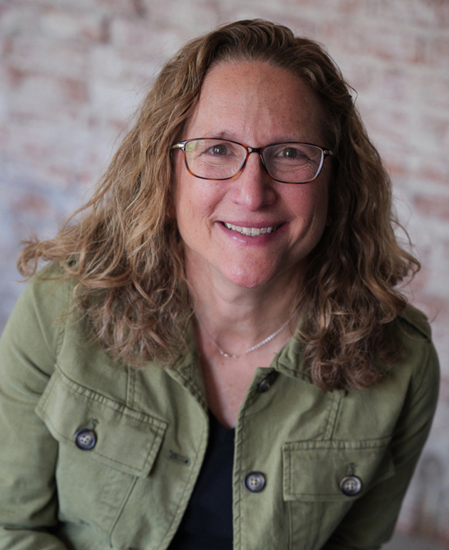 A portrait of Karen Handelman with shoulder length hair, dark framed glasses, and a green jacket.