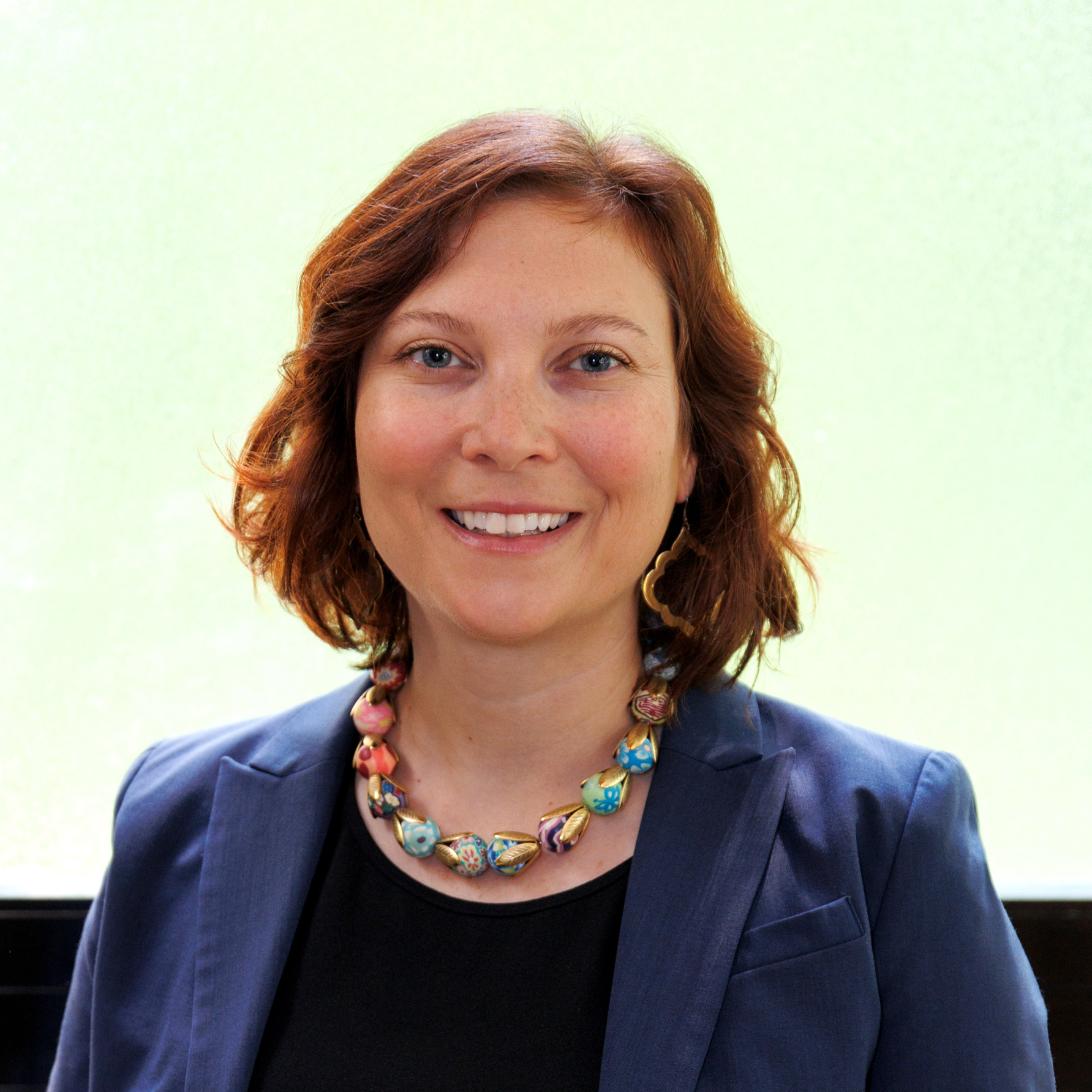 A woman with shoulder length hair wearing a blazer.