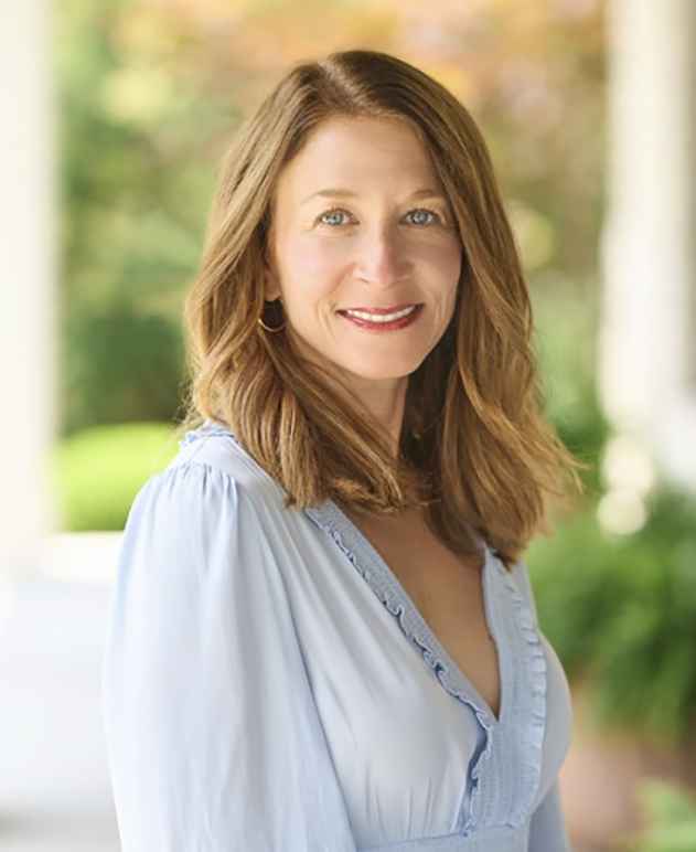 A woman with shoulder length hair wearing a blouse. 