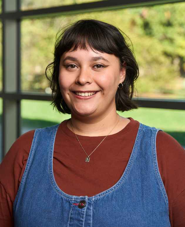 a woman with dark hair wearing a brown shirt and denim dress