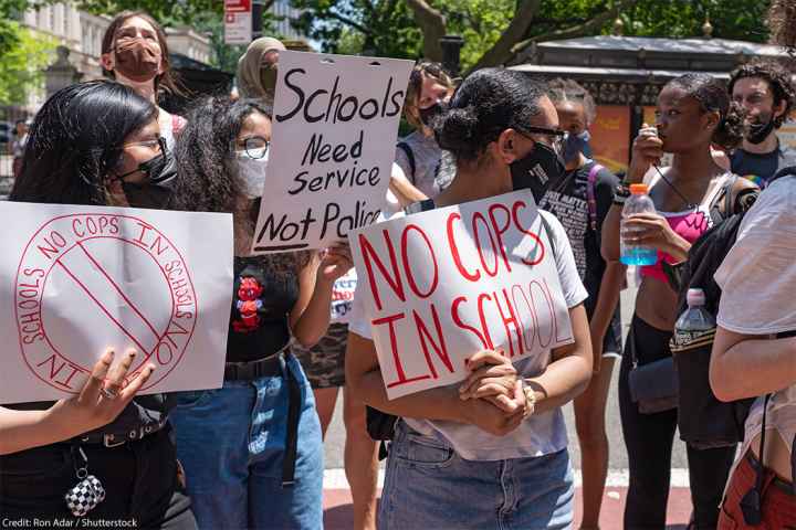 Demonstrators holding signs that read "No Cops In Schools" and "Schools Need Service Not Police" protest outside City Hall in New York City.
