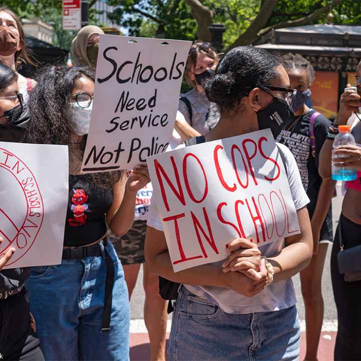 Demonstrators holding signs that read "No Cops In Schools" and "Schools Need Service Not Police" protest outside City Hall in New York City.