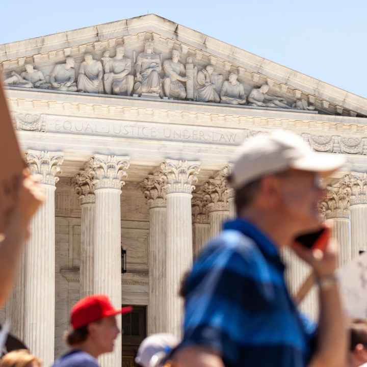 Pro-choice demonstrators (whose faces and signs are blurred) march in front of the Supreme Court and the statement on its facade, "Equal justice under law".