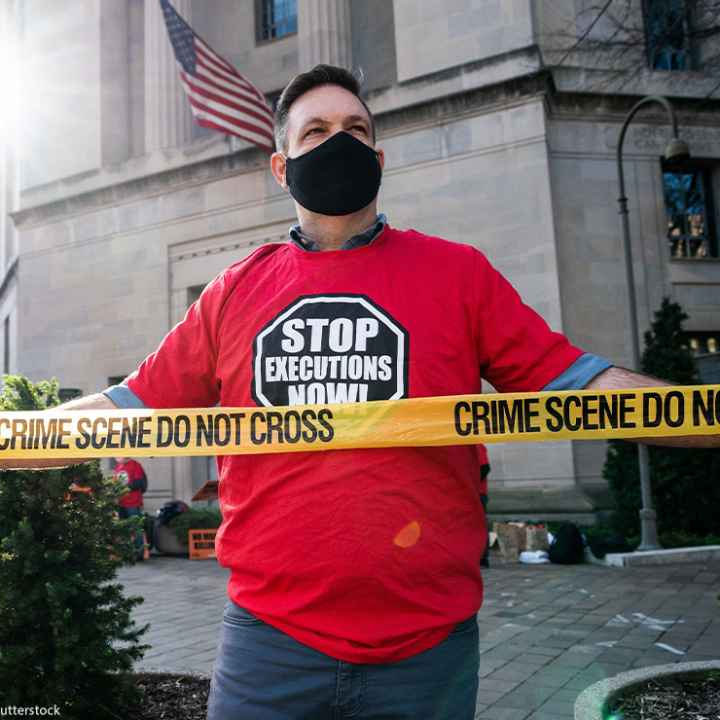 Man protesting against the death penalty in fron of the U.S. Justice Dept wearing a red shirt with a black stop sign reading "STOP EXECUTIONS NOW" in white letters.
